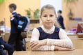 Portrait of schoolgirl sitting at desk in classroom at recess while other schoolkids playing Royalty Free Stock Photo