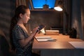 Portrait of schoolgirl using doing homework writing in notebook sitting at desk at evening, holding and using tablet pad Royalty Free Stock Photo