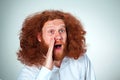 Portrait of screaming young man with long red hair and shocked facial expression on gray background Royalty Free Stock Photo