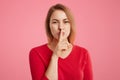 Portrait of secret beautiful young woman keeps fore finger on lips, shows silence sign, tries to keep personal information in secr Royalty Free Stock Photo