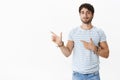 Portrait of self-assured good-looking tanned young caucasian male with bristle, blue eyes in striped t-shirt pointing