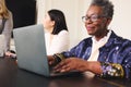 Portrait of senior black businesswoman with short gray hair wearing glasses and using laptop Royalty Free Stock Photo