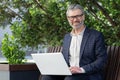 Portrait of senior businessman outdoors in park on bench, mature boss smiling and looking at camera, man in suit working Royalty Free Stock Photo