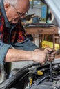 Portrait of a senior car mechanic changing spark plugs on his old car in the garage.