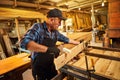 Portrait of a senior carpenter in uniform gluing wooden bars with hand pressures at the carpentry manufacturing