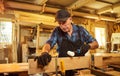 Portrait of a senior carpenter in uniform gluing wooden bars with hand pressures at the carpentry manufacturing