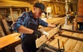 Portrait of a senior carpenter in uniform gluing wooden bars with hand pressures at the carpentry manufacturing