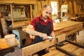 Portrait of a senior carpenter in uniform gluing wooden bars with hand pressures at the carpentry manufacturing