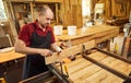 Portrait of a senior carpenter in uniform gluing wooden bars with hand pressures at the carpentry manufacturing