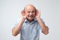 Portrait of senior casual man which overhears conversation over white background. Speak loudly please concept. Royalty Free Stock Photo