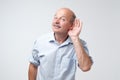 Portrait of senior casual man which overhears conversation over white background. Speak loudly please concept. Royalty Free Stock Photo