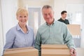 Portrait Of Senior Couple Downsizing In Retirement Carrying Boxes Into New Home On Moving Day With Removal Man Helping