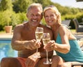 Portrait Of Senior Couple On Holiday In Swimming Costumes Drinking Champagne By Hotel Swimming Pool Royalty Free Stock Photo