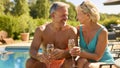 Portrait Of Senior Couple On Holiday In Swimming Costumes Drinking Champagne By Hotel Swimming Pool Royalty Free Stock Photo