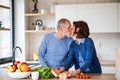 A portrait of senior couple in love indoors at home, kissing when cooking.