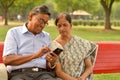 Portrait of senior couple sitting in park bench and looking at their smart phone and laughing in New Delhi, India with focus on Royalty Free Stock Photo