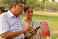 Portrait of senior couple sitting in park bench and looking at their smart phone and laughing in New Delhi, India with focus on Royalty Free Stock Photo