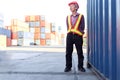 Portrait of senior elderly Asian worker engineer wearing safety vest and helmet, standing at logistic shipping cargo containers