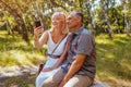 Portrait of senior family couple taking selfie using smartphone in summer forest. Elderly people rest sitting on bench Royalty Free Stock Photo