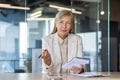 Portrait of a senior gray-haired businesswoman in a suit sitting in the office at a desk, holding a notebook with a pen Royalty Free Stock Photo