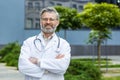 Portrait of senior gray-haired doctor, mature man in white medical coat with crossed arms and stethoscope smiling and Royalty Free Stock Photo