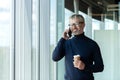 Portrait of a senior handsome gray-haired man designer, architect, engineer standing in the office by the window talking Royalty Free Stock Photo