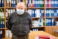 Portrait of senior male archivist with hands behind back looking at camera, man wearing facial mask due coronavirus pandemic, Royalty Free Stock Photo