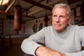 Portrait Of Senior Male Boxing Coach In Gym Standing By Old Fashioned Leather Punching Bags