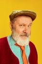 Portrait of senior man in classical clothes, glasses and cap posing over vivid yellow background. Curious, serious look