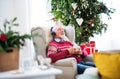 A portrait of senior man with headphones sitting on armchair at home at Christmas time. Royalty Free Stock Photo