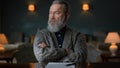 Portrait of senior man sitting at table with crossed hands in vintage cabinet. Royalty Free Stock Photo