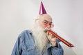 Portrait of senior man wearing party hat while blowing horn against gray background
