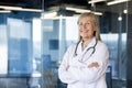 Portrait of senior mature female doctor in white medical coat, head doctor of clinic with arms crossed smiling and Royalty Free Stock Photo
