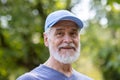 Portrait of senior mature gray-haired man in park, pensioner in sports cap smiling and looking at camera close-up among Royalty Free Stock Photo