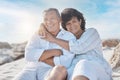 Portrait of a senior mixed race couple sitting together on the beach embracing one another and smiling on a day out at Royalty Free Stock Photo