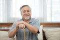 Portrait of senior old elderly asian man sit on coach hand hold help walking stick sit on sofa in house look at camera with