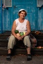 Portrait of senior old woman sitting on doorstep of her house with crop of vegetables in her hands. Elderly happiness