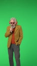 Portrait of senior stylish hipster on Chroma key green screen background, man in headphones sings in microphone