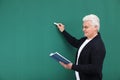 Portrait of senior teacher with book and chalk at green board Royalty Free Stock Photo