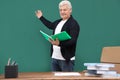 Portrait of senior teacher with notebook at green chalkboard