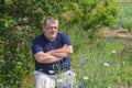 Portrait of senior Ukrainian peasant sitting in a spring garden and admiring Centaurea flowers