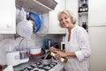 Portrait of senior woman adding olive oil to saucepan at kitchen counter