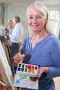 Portrait Of Senior Woman Attending Painting Class With Teacher          In Background Royalty Free Stock Photo