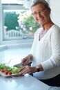 Portrait of senior woman on chopping board, vegetables and knife in kitchen cooking food. Happy person in glasses