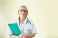 Portrait senior woman doctor standing holding folder with stethoscope near yellow background at hospital Royalty Free Stock Photo