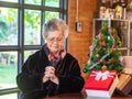 Portrait of a senior woman with eyes closed praying and sitting near a Christmas tree at home. Concept of aged people and festival Royalty Free Stock Photo