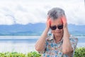 Portrait of a senior woman feeling headache while sitting at the side of the lake. Brain diseases problem cause chronic severe