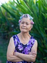 Portrait of senior woman hair curlers, arms crossed and looking at the camera while standing in a garden. Space for text. Royalty Free Stock Photo