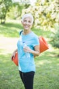 Portrait of senior woman holds fitness mat on her back in the park and preparing for exercise Royalty Free Stock Photo