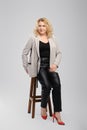 Portrait of senior woman in leather trousers and blazer sitting on tall wooden chair Royalty Free Stock Photo